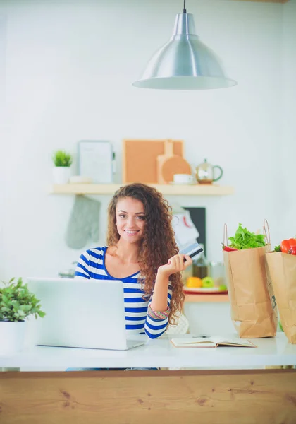 Leende ung kvinna med kaffekopp och laptop i köket hemma. Leende ung kvinna — Stockfoto