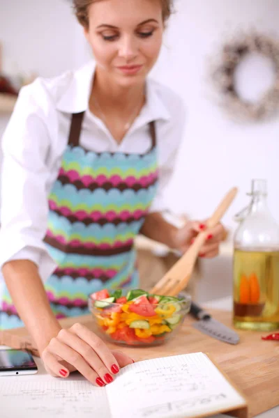 Улыбающаяся молодая женщина готовит салат на кухне . — стоковое фото