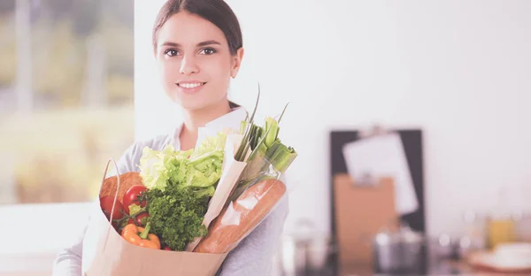 Молодая женщина держит сумку с овощами. Стоя на кухне — стоковое фото