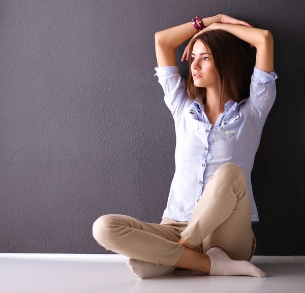 Młoda kobieta siedząca na podłodze przy ciemnej ścianie — Zdjęcie stockowe
