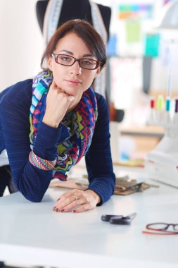 Güzel moda tasarımcısı stüdyoda masada oturuyor. .