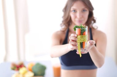 Elinde bir bardak dolusu taze meyve salatası ve bardağın etrafında mezura tutan bir kadın..