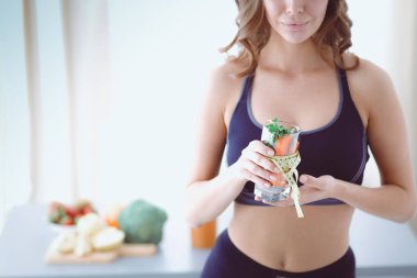 Elinde bir bardak dolusu taze meyve salatası ve bardağın etrafında mezura tutan bir kadın..