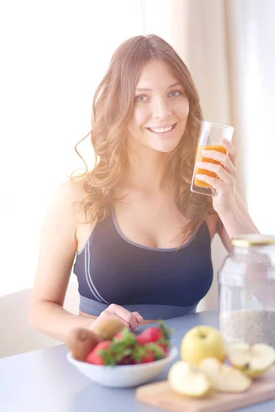 Chica sentada en la cocina en el escritorio con frutas y vasos con jugo . — Foto de Stock