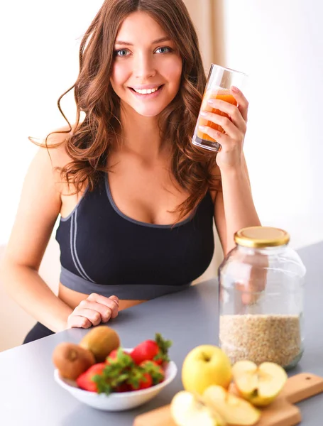 Chica sentada en la cocina en el escritorio con frutas y vasos con jugo —  Fotos de Stock
