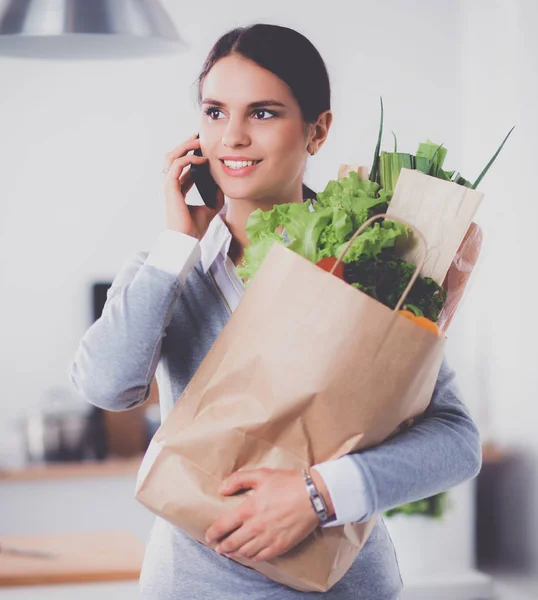 Giovane donna che tiene la borsa della spesa con verdure. In piedi in cucina — Foto Stock