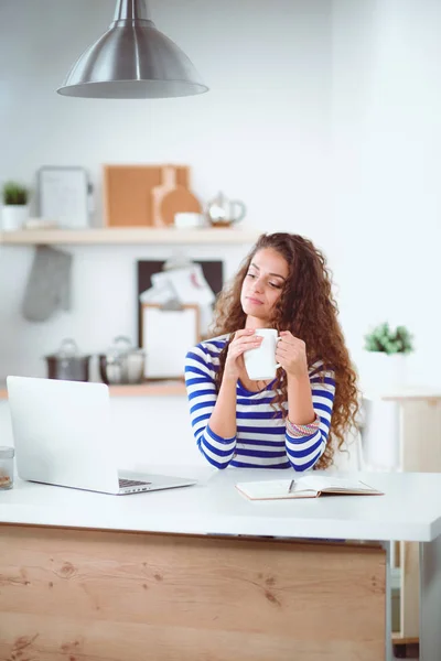 コーヒー カップと自宅の台所でラップトップを持つ若い女性の笑みを浮かべてください。若い女性の笑顔 — ストック写真