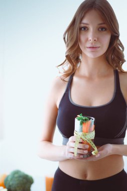 Elinde bir bardak dolusu taze meyve salatası ve bardağın etrafında mezura tutan bir kadın..