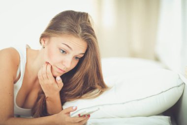 Güzel genç kadın yatağında yatan bir kısa mesaj okuma.