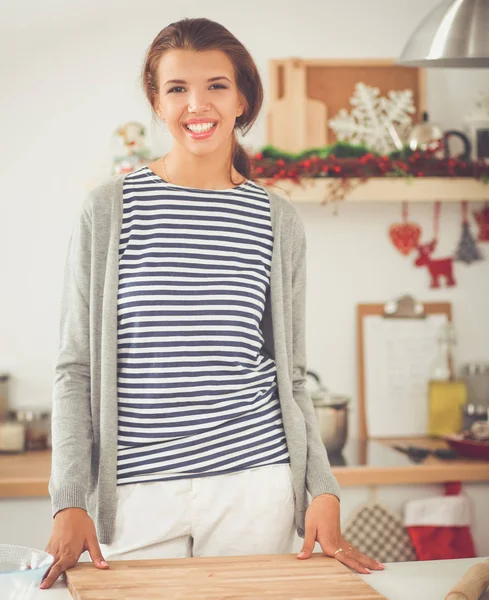 Glimlachende jonge vrouw in de keuken, geïsoleerd op kerst achtergrond — Stockfoto