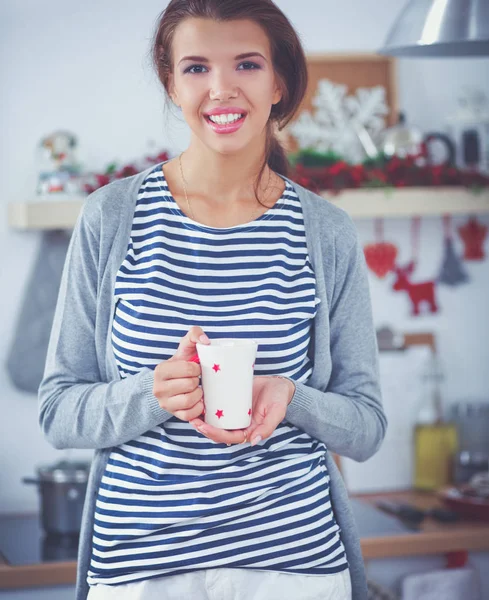 Portret van jonge vrouw met kopje tegen keuken interieur achtergrond. — Stockfoto