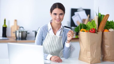 Mutfakta bilgisayar ve kredi kartı kullanan gülümseyen bir kadın.