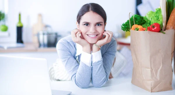 Schöne junge Frau kocht mit Blick auf Laptop-Bildschirm mit Quittung in der Küche — Stockfoto