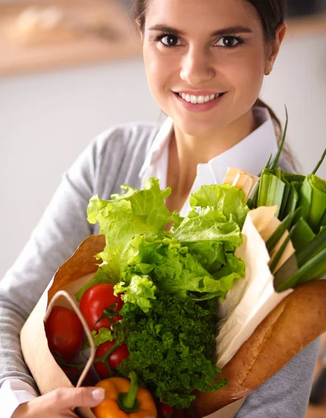 Jeune femme tenant un sac d'épicerie avec des légumes Debout dans la cuisine. — Photo