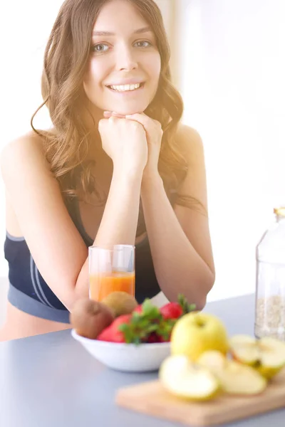 Flicka sitter i köket på skrivbord med frukt och glas med juice. — Stockfoto