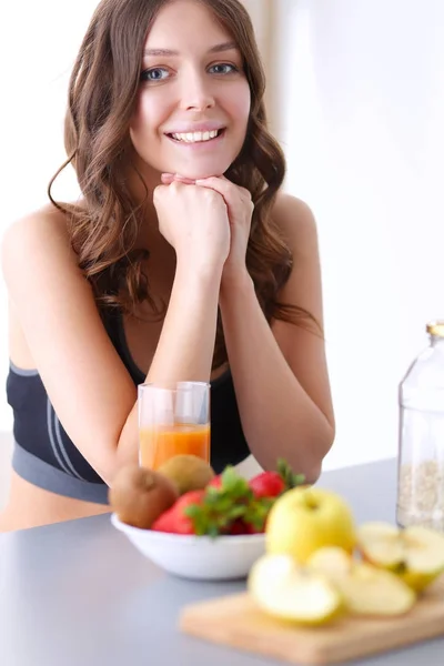 Chica sentada en la cocina en el escritorio con frutas y vasos con jugo . — Foto de Stock