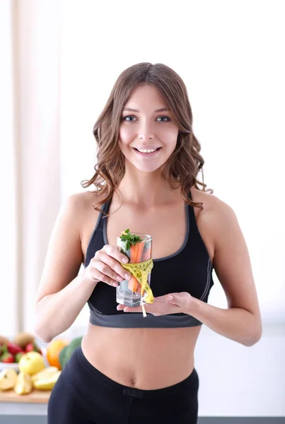 Mujer sosteniendo un vaso lleno de ensalada de frutas frescas con una cinta métrica alrededor del vaso. — Foto de Stock