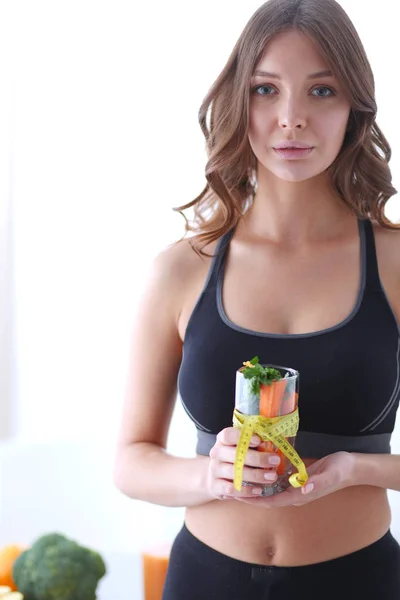 Mujer sosteniendo un vaso lleno de ensalada de frutas frescas con una cinta métrica alrededor del vaso. —  Fotos de Stock