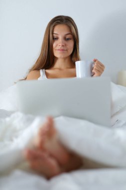 Yatak ve çay tadını çıkarırken bir dizüstü bilgisayar ile genç ve güzel bir kadın