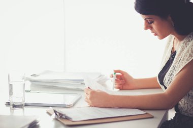 Elinde evrakları olan kadın masanın üstünde oturuyor.