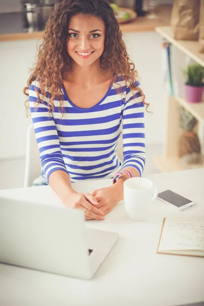 Χαμογελώντας νεαρή γυναίκα με φλιτζάνι καφέ και το φορητό υπολογιστή στην κουζίνα στο σπίτι. Χαμογελώντας νεαρή γυναίκα — Φωτογραφία Αρχείου