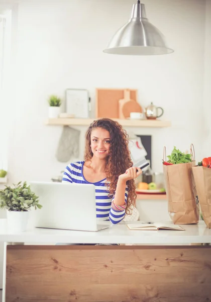 Lachende jonge vrouw met koffiekopje en laptop in de keuken thuis. Lachende jonge vrouw — Stockfoto