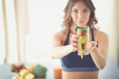 Elinde bir bardak dolusu taze meyve salatası ve bardağın etrafında mezura tutan bir kadın..