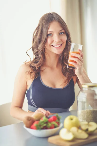 Chica sentada en la cocina en el escritorio con frutas y vasos con jugo . — Foto de Stock