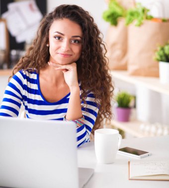 kahve fincanı ve dizüstü evde mutfakta gülümseyen genç kadın