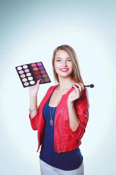 Jeune belle femme tient dans une main et une palette avec de la peinture et des ombres pour le maquillage, brosse d'occasion pour le maquillage. — Photo