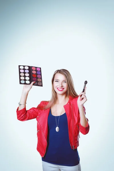 Jeune belle femme tient dans une main et une palette avec de la peinture et des ombres pour le maquillage, brosse d'occasion pour le maquillage. — Photo