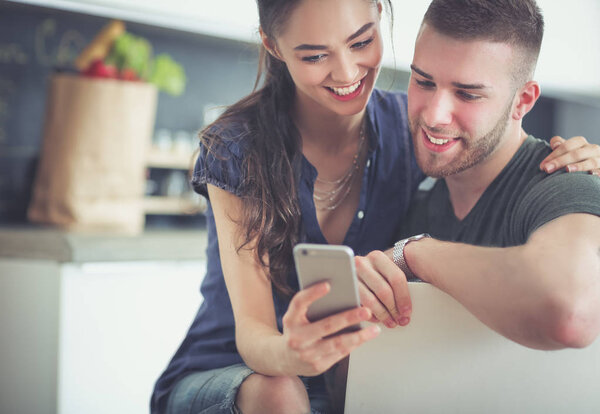 Happy couple using smartphone sitting in kitchen.