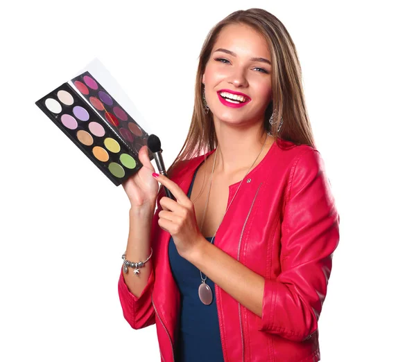 Young beautiful woman holds in one hand and a palette with paint and shadows for makeup, second hand brush for makeup — Stock Photo, Image
