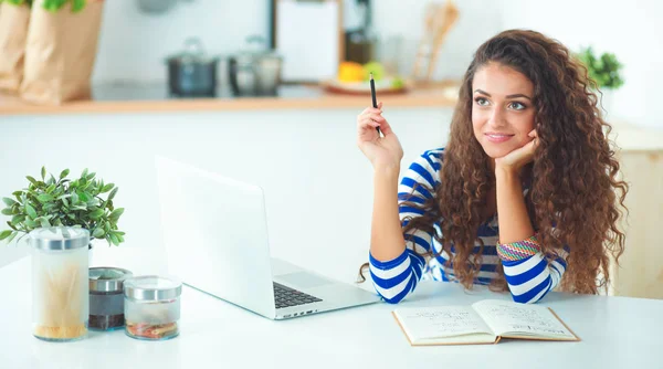 Lachende jonge vrouw met koffiekopje en laptop in de keuken thuis — Stockfoto