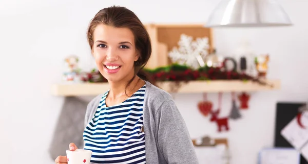 Glimlachende jonge vrouw in de keuken, geïsoleerd op kerst achtergrond — Stockfoto