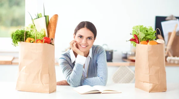 Młoda kobieta trzyma torbę na zakupy z warzywami. Stojąc w kuchni — Zdjęcie stockowe