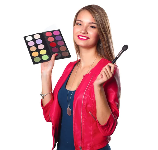 Giovane bella donna tiene in una mano e una tavolozza con vernice e ombre per il trucco, spazzola di seconda mano per il trucco — Foto Stock