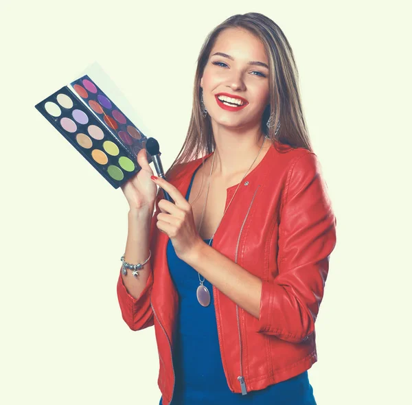 Joven hermosa mujer sostiene en una mano y una paleta con pintura y sombras para el maquillaje, cepillo de segunda mano para maquillaje — Foto de Stock