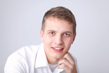 Gri arka plan üzerinde oturan gülümseyen genç adam portresi. Genç adam portresi