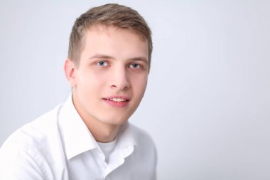 Gri arka plan üzerinde oturan gülümseyen genç adam portresi. Genç adam portresi