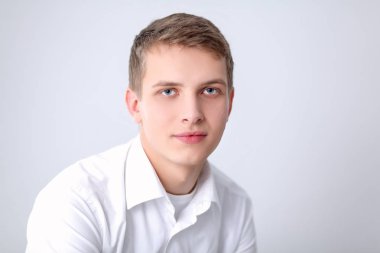 Gri arka plan üzerinde oturan gülümseyen genç adam portresi. Genç adam portresi