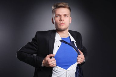 Genç işadamı hareket ve bir süper kahraman gibi gömleğini, yırtılma gri arka plan üzerinde izole. Genç işadamı