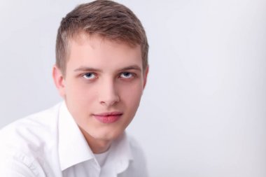 Gri arka plan üzerinde oturan gülümseyen genç adam portresi. Genç adam portresi