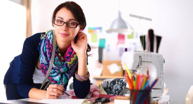 Güzel moda tasarımcısı stüdyoda masada oturuyor.