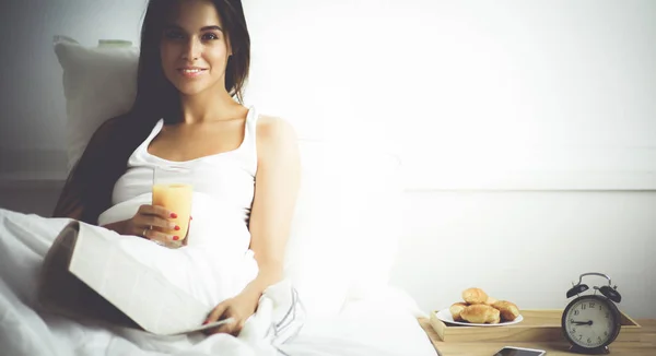 Όμορφη νεαρή γυναίκα κάθεται στο κρεβάτι και τρώει πρωινό — Φωτογραφία Αρχείου