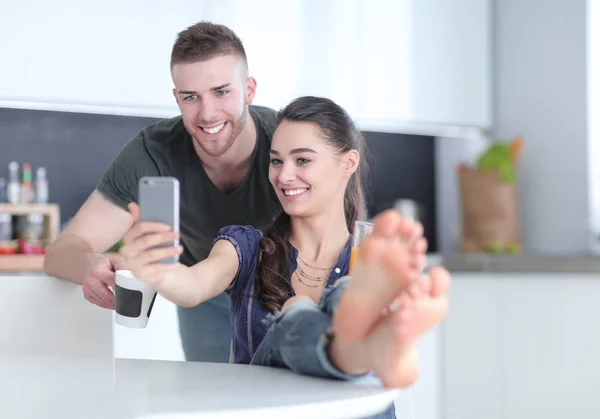 Mutlu çift mutfakta oturmuş smartphone kullanarak — Stok fotoğraf