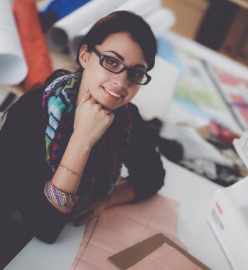 Güzel moda tasarımcısı stüdyoda masada oturuyor.