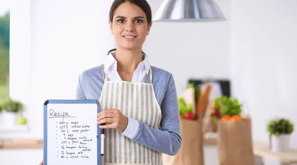 Mujer en la cocina en casa, de pie cerca de escritorio con carpeta —  Fotos de Stock