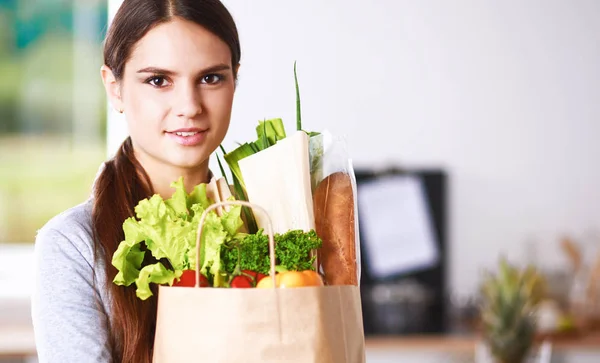 Giovane donna che tiene la spesa con verdure In piedi in cucina. — Foto Stock