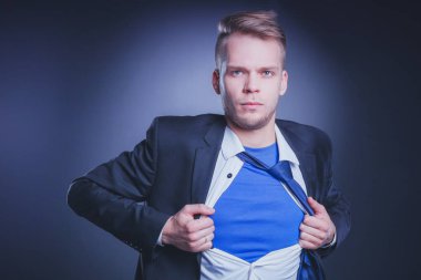 Genç işadamı hareket ve bir süper kahraman gibi gömleğini, yırtılma gri arka plan üzerinde izole. Genç işadamı